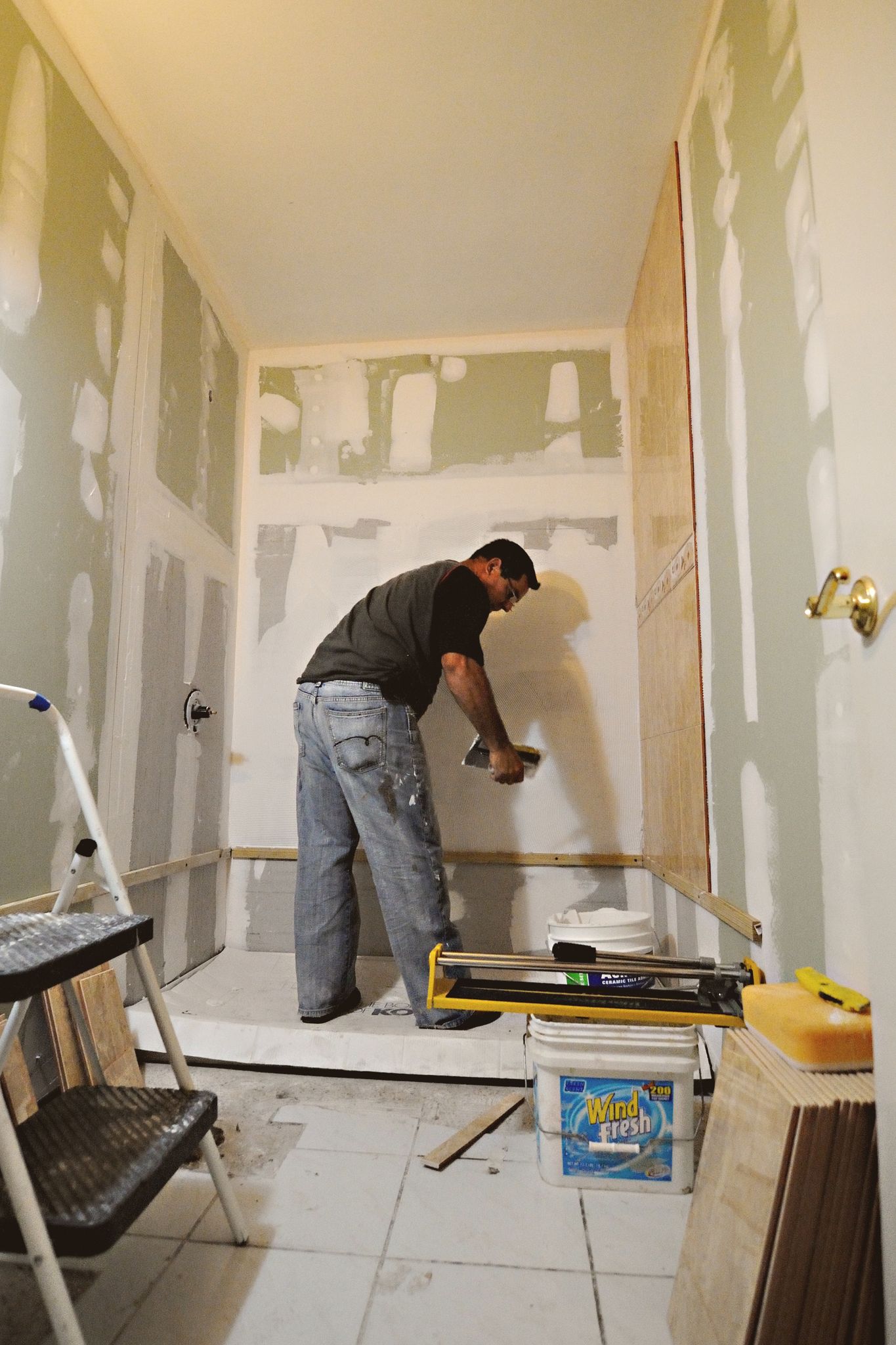 A man working on a bathroom renovation, applying drywall mud on interior walls.